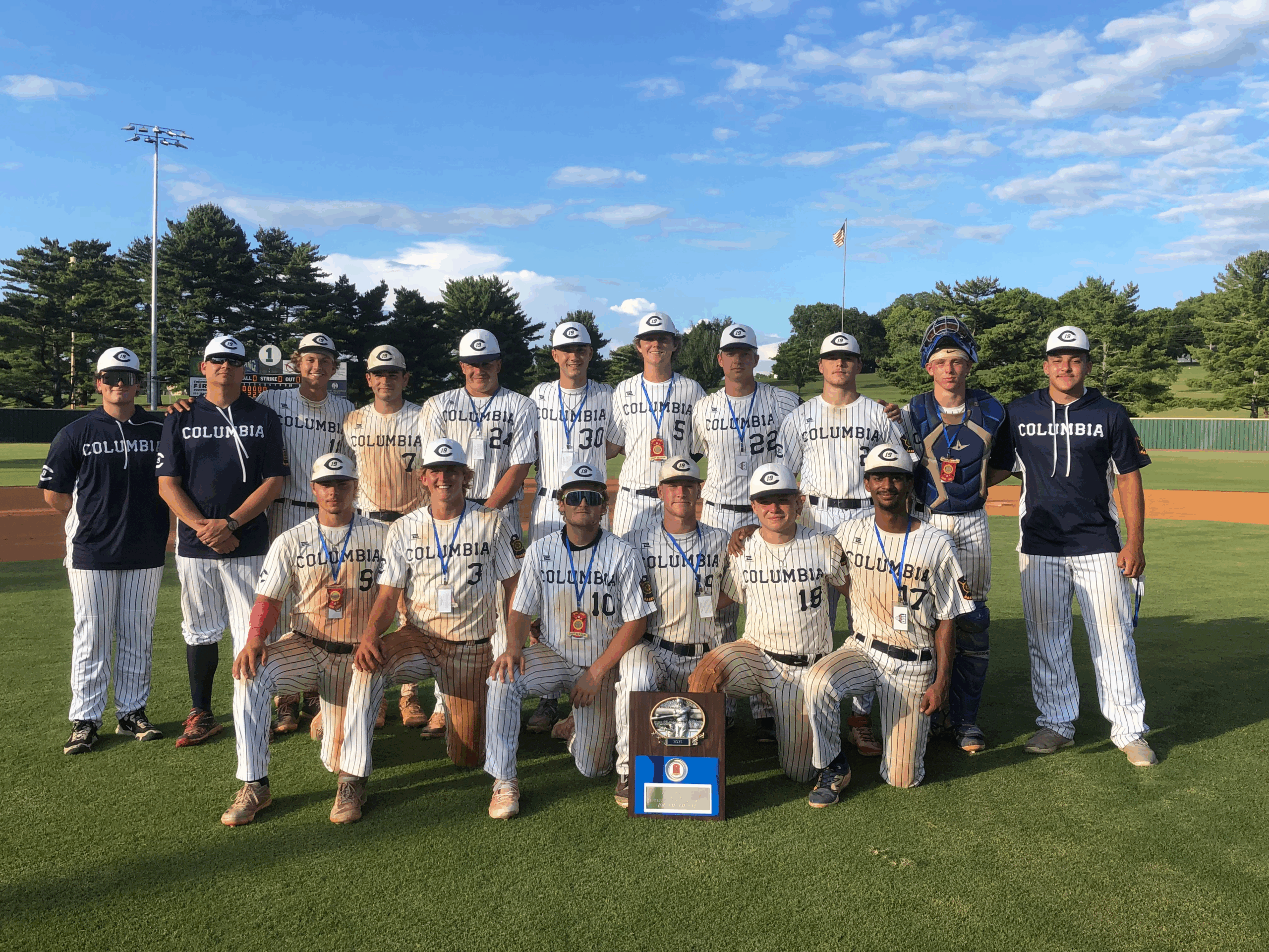 Columbia's baseball team poses triumphantly on a field, wearing striped uniforms and medals, celebrating a championship win.
